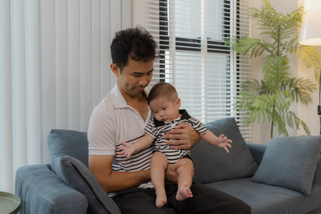 A cheerful father bonding with his baby in the living room, smiling warmly while holding the infant...