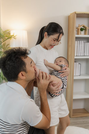 A young family shares tender moments with their baby in a cozy home. The father kisses the baby tiny...