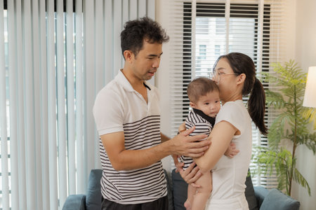 A young family shares tender moments with their baby in a cozy home. The father kisses the baby tiny...