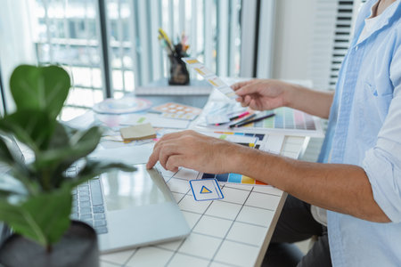 A designer is working on a creative UX UI project at a desk, arranging color palettes and layout...