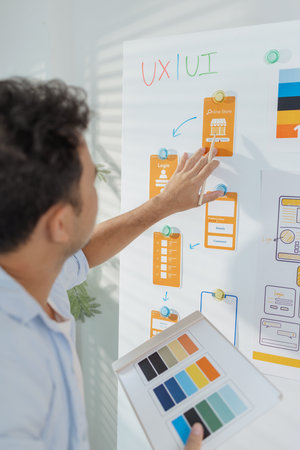 A young designer is working on a UX UI project, analyzing mobile app wireframes and choosing color...