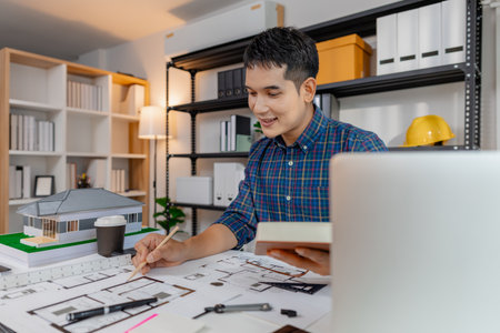 Young architect working in office with building models and floor plans, analyzing details and...