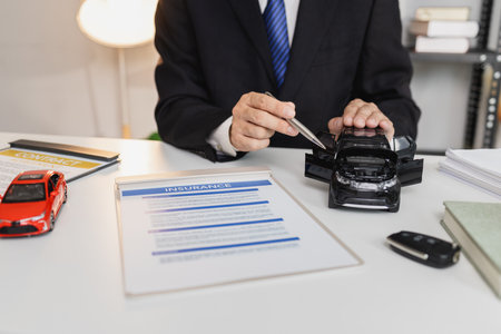 A businessman in a suit is presenting car insurance and contract documents with miniature car models...