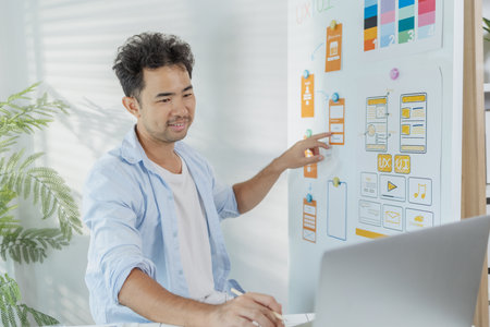 A young designer is working on a UX UI project, analyzing mobile app wireframes and choosing color...
