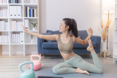 A young woman practices yoga at home on a mat, performing stretching, meditation, and strength poses...
