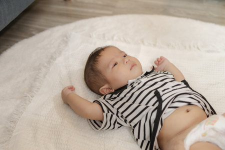 A close-up shot of an adorable baby lying on a soft white blanket, wearing a striped onesie, looking...