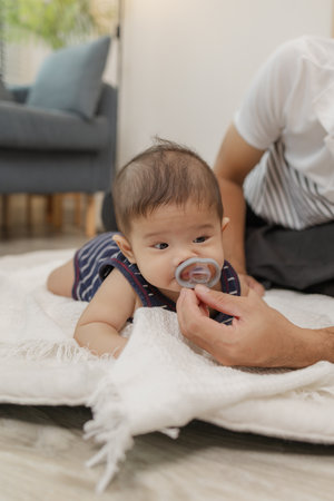 A father spends quality time with his baby, playing and bonding through gentle care and fun moments on a soft mat. The baby explores tummy time and pacifier use with support.の写真素材