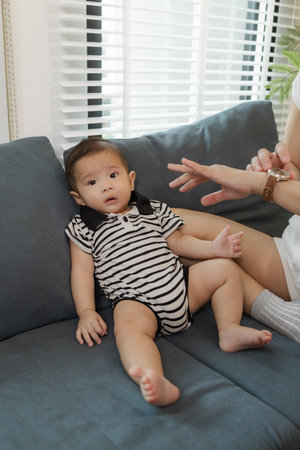 A mother lovingly interacts with her baby while lying on the sofa, creating a warm and tender...