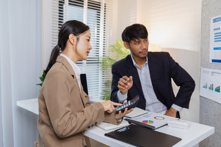 Business colleagues are engaged in a collaborative discussion, analyzing financial charts and reports on the wall and table. They exchange ideas, review strategies, and plan future goals.の写真素材