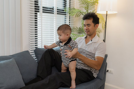 A tender moment of a father holding his baby, as the infant looks up with curiosity and trust. The warm interaction reflects family love, bonding, and parental care.の写真素材