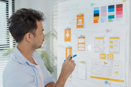 A young designer is working on a UX UI project, analyzing mobile app wireframes and choosing color...