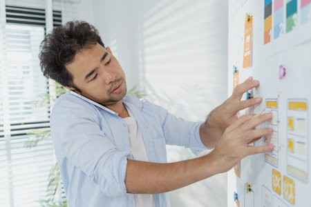 A creative designer works on UX/UI planning, analyzing sketches and prototypes on a whiteboard while using a laptop. The process shows design thinking, user flow, and digital innovation.の写真素材