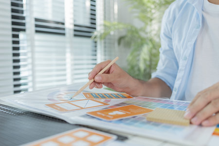 A focused designer is working on UX/UI design ideas, analyzing color palettes and interface structures pinned on a board. The scene reflects creativity, planning, and digital innovation.の写真素材