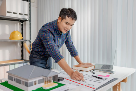 A young architect is multitasking at his desk, sketching blueprints, making phone calls, and...