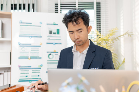 A businessman in a suit analyzing financial charts and performance reports in a bright modern office, focusing on strategy, data, and budget planning for company growth and long-term success.の写真素材