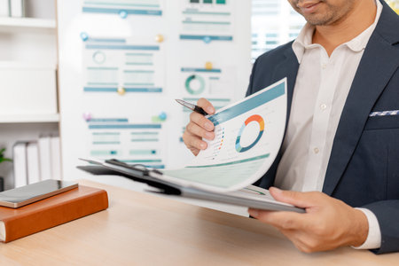 A confident businessman calculating budget and reviewing company performance using reports and charts in a clean modern office, focusing on financial goals, investments, and strategic success.の写真素材