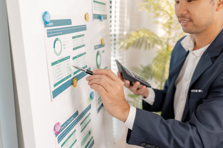 A business analyst examining charts and statistics on a whiteboard, using data-driven insights to guide financial strategy, business performance, and future organizational planning.の写真素材