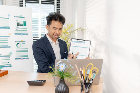A confident businessman calculating budget and reviewing company performance using reports and charts in a clean modern office, focusing on financial goals, investments, and strategic success.の写真素材