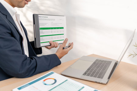 A confident businessman calculating budget and reviewing company performance using reports and charts in a clean modern office, focusing on financial goals, investments, and strategic success.の写真素材