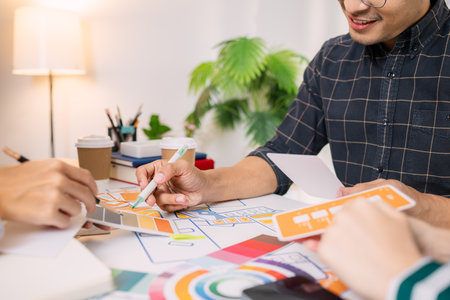 Designers having a UX/UI planning meeting to refine mobile app layouts and user flow. They collaborate closely to create functional and visually appealing interface solutions.の写真素材