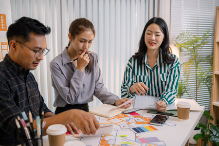 Designers having a UX/UI planning meeting to refine mobile app layouts and user flow. They collaborate closely to create functional and visually appealing interface solutions.の写真素材