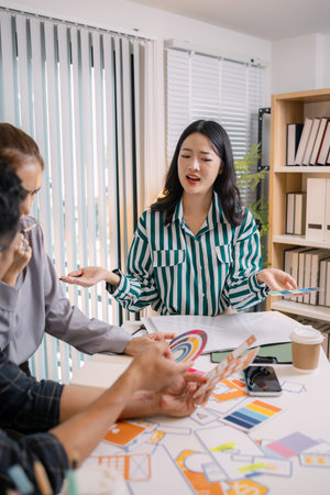 Designers having a UX/UI planning meeting to refine mobile app layouts and user flow. They collaborate closely to create functional and visually appealing interface solutions.の写真素材