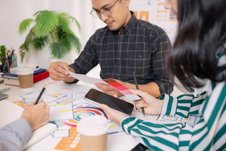 A group of UX/UI designers brainstorming creative ideas together, discussing color palettes and layout concepts for a new mobile application interface in a modern design office.の写真素材