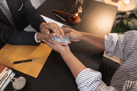 An unethical act of bribery showing hands exchanging cash in a law office environment, symbolizing...