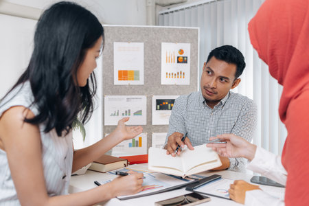 A group of multicultural colleagues in a modern office discussing data and marketing reports. The...