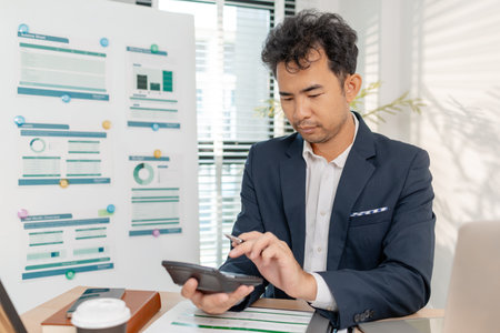 A businessman in a suit analyzing financial charts and performance reports in a bright modern office, focusing on strategy, data, and budget planning for company growth and long-term success.の写真素材