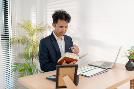 A businessman preparing a marketing and financial plan in a modern office, reviewing charts and data reports to support company strategy, performance growth, and organizational efficiency.の写真素材