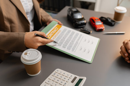 A business meeting between a car dealer and a client discussing vehicle purchase agreement. The contract is being reviewed and explained before signing, representing trust and cooperation.の写真素材