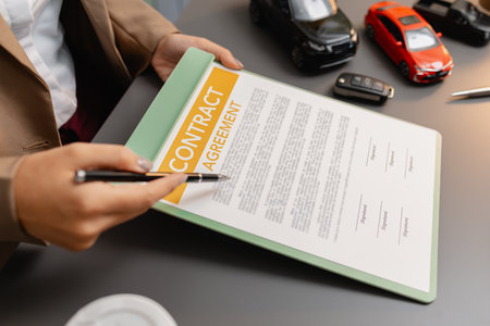 A business meeting between a car dealer and a client discussing vehicle purchase agreement. The contract is being reviewed and explained before signing, representing trust and cooperation.の写真素材
