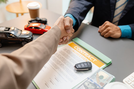 A car sales representative and a customer shake hands after signing a vehicle purchase contract. The handshake reflects satisfaction, trust, and successful completion of the car deal.の写真素材