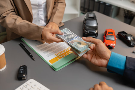A businessperson and client are reviewing and signing a car sales contract at a desk, with small...