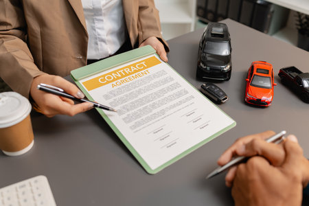 A business meeting between a car dealer and a client discussing vehicle purchase agreement. The contract is being reviewed and explained before signing, representing trust and cooperation.の写真素材