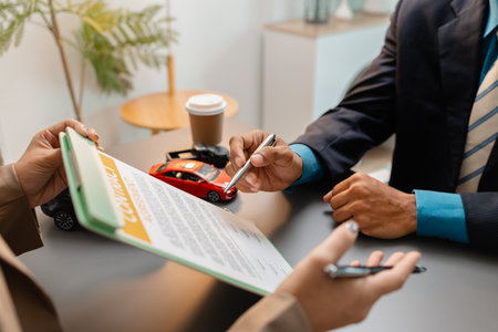 A business meeting between a car dealer and a client discussing vehicle purchase agreement. The contract is being reviewed and explained before signing, representing trust and cooperation.の写真素材