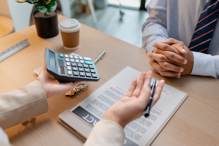 A real estate agent and a client are discussing and pointing at a housing contract document during a property purchase meeting, showing agreement details and financial negotiation about home ownershipの写真素材