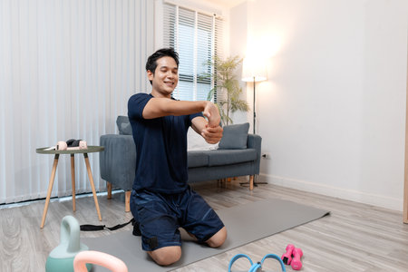 A young man exercising at home in a cozy living room, focusing on his health and fitness. He enjoys his daily workout routine, surrounded by simple gym equipment that supports a balanced lifestyle.の写真素材