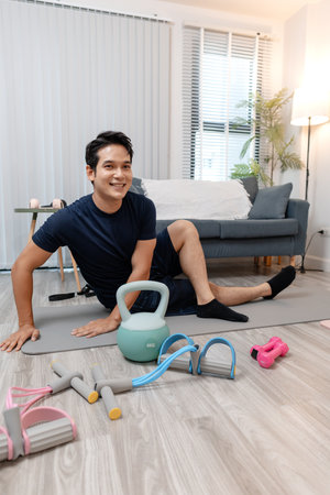A young man exercising at home in a cozy living room, focusing on his health and fitness. He enjoys his daily workout routine, surrounded by simple gym equipment that supports a balanced lifestyle.の写真素材
