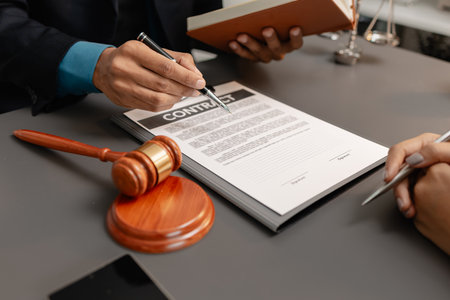 A male lawyer in a suit discusses contract details with a female client, pointing to the signature...