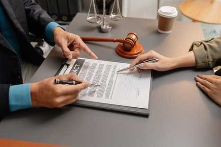 A male lawyer in a suit discusses contract details with a female client, pointing to the signature...