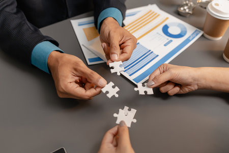 Business people holding puzzle pieces together on the office desk, symbolizing teamwork,...