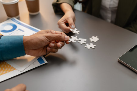 Business people holding puzzle pieces together on the office desk, symbolizing teamwork, collaboration, planning, and strategy development for effective organizational management.の写真素材