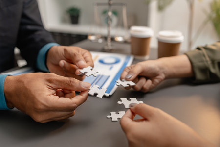 Business people holding puzzle pieces together on the office desk, symbolizing teamwork, collaboration, planning, and strategy development for effective organizational management.の写真素材