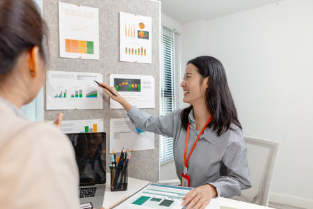 Two Asian businesswomen discussing company strategy together in a modern office, analyzing financial documents and charts. They are collaborating and sharing ideas for future business development.の写真素材