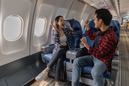 Excited couple celebrating together while sitting on an airplane. Their cheerful expressions and body language suggest joy and enthusiasm about their journey or shared travel experience.の写真素材