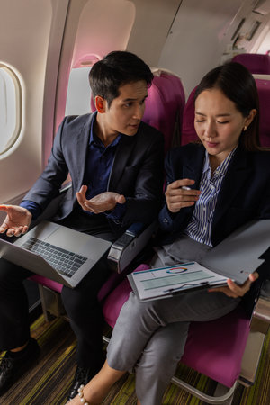 A stressful moment during a flight where a manager appears to be discussing work with his secretary. The woman looks upset and overwhelmed while holding documents in a tense discussion.の写真素材