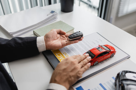 A businessman in a suit is presenting car insurance and contract documents with miniature car models on the desk, symbolizing vehicle insurance, financial planning, and legal agreements.の写真素材