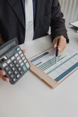 A businessman in a suit is calculating car loan options using a calculator and comparison chart, with model cars and car keys on the desk, symbolizing finance, leasing, and investment planning.の写真素材